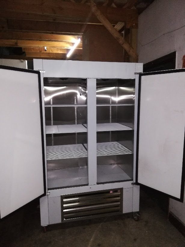 An Cooltech Stainless Steel 2-Door Reach-In Cooler 48” with empty shelves in a dimly lit storage room.