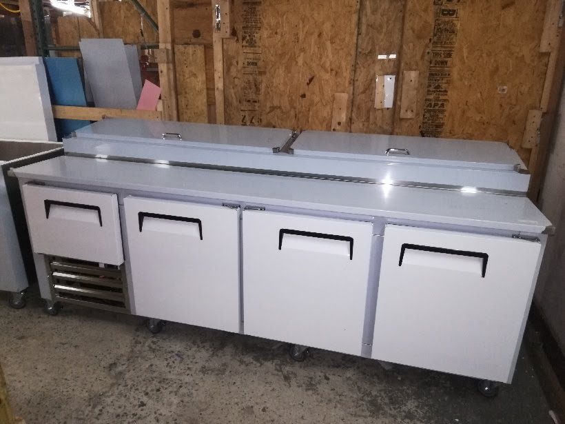A Cooltech 3-1/2 Door Refrigerated Pizza Prep Table 96" with multiple drawers and a stainless steel countertop in a storage room.