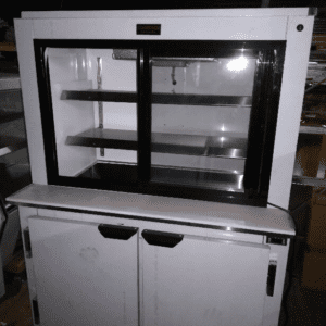 A Cooltech Pass-Through Display Pie Case Refrigerator 36'' with sliding glass doors on top and closed storage cabinets below, set in a dimly lit storage area.